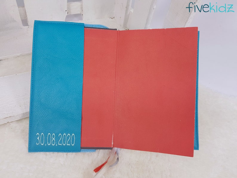Puede incluir: Un diario de tapa dura de color azul turquesa con interior rojo y la fecha "30.08.2020" bordada en la portada.