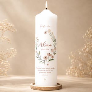 Könnte beinhalten: Eine weiße Stumpenkerze mit brennendem Docht, verziert mit einem Blumenkranz in zarten Rosa- und Grüntönen. Der Text lautet "Taufe von Alma 07.05.2024" und enthält einen Bibelvers aus Psalm 91, 11, sowie ein kleines Kreuzsymbol am unteren Rand.