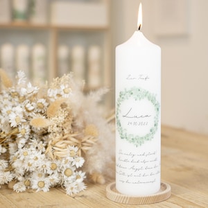 May include: White baptism candle with a green eucalyptus wreath design. The candle has the name "Luca" and the date "26.10.2022" printed on it. The text "Zur Taufe" is also printed on the candle.