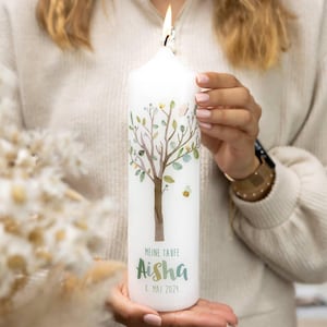 Könnte beinhalten: Eine brennende weiße Kerze mit einem Baumdesign, einer Biene und dem Namen "Aisha" in grüner Schrift. Der Text "MEINE TAUFE" und das Datum "8. MAI 2024" sind ebenfalls sichtbar. Die Kerze wird von einer Person gehalten.