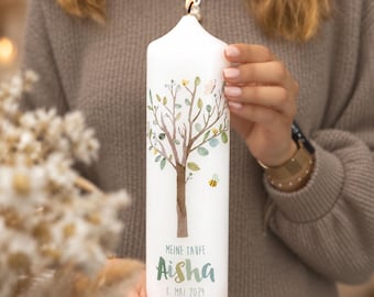 May include: A white pillar candle with a lit flame, featuring a watercolour illustration of a tree with green leaves, a small butterfly, and a bee. The text reads MEINE TAUFE, Aisha, and 8. MAI 2024 in green and grey lettering on the front.