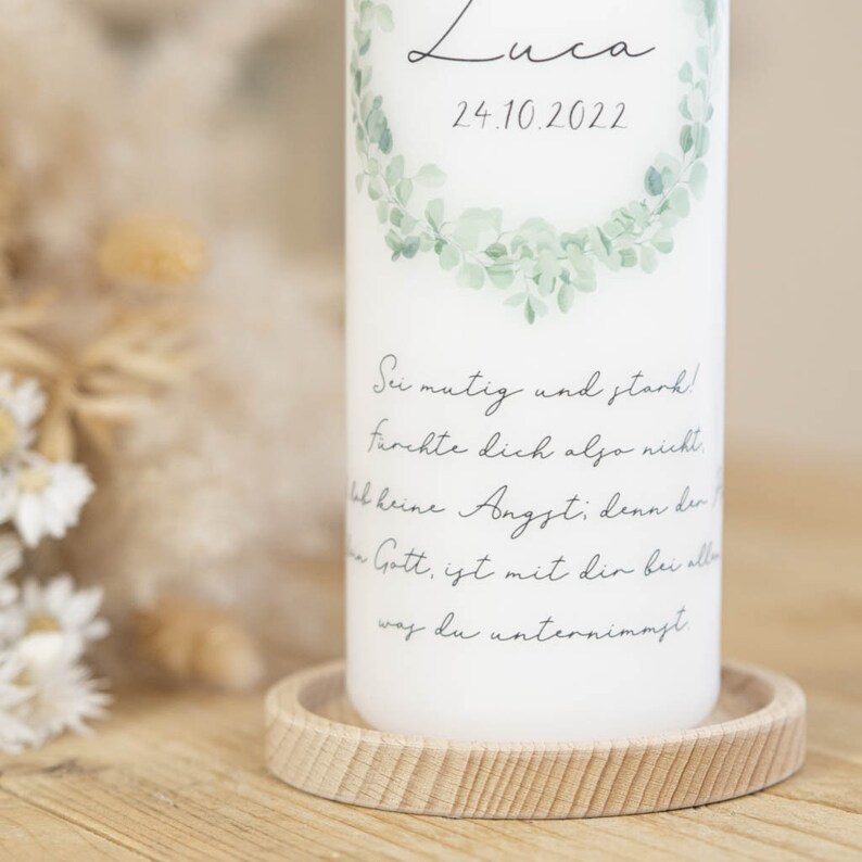 May include: White candle with a green leafy wreath design and the text "Luca 24.10.2022". The candle also has the text "Sei mutig und stark! Furchte dich also nicht. Hab keine Angst; denn der Herr Gott, ist mit dir bei allem was du unternimmst."