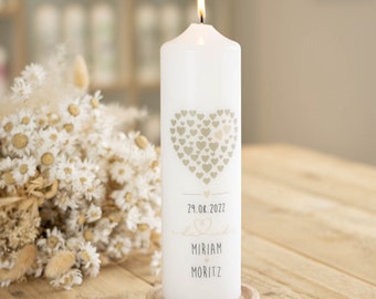 May include: White pillar candle with a gold heart design and the text "29.08.2022 Miriam & Moritz" on the side.