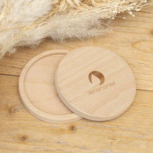 Puede incluir: Dos posavasos redondos de madera con un acabado de madera natural. El posavasos superior tiene el texto "kerzenonkel" y un dise&ntilde;o de llama estilizado.
