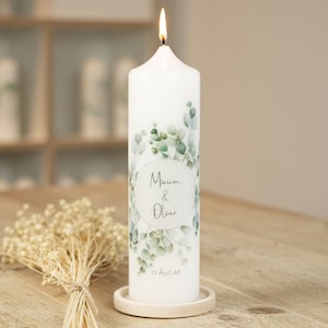 May include: White pillar candle with a green eucalyptus leaf design and the text "Miriam & Oliver 23 August 2023".