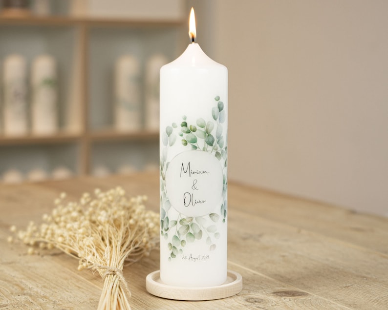 May include: White pillar candle with a green eucalyptus leaf design and the text "Miriam & Oliver 23 August 2023".
