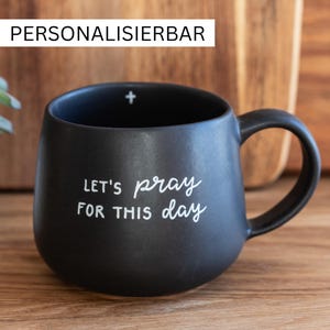 Könnte beinhalten: Eine mattschwarze Keramiktasse mit abgerundeter Form und Henkel. Auf der Vorderseite steht der weiße Text "LET'S pray FOR THIS day" in einer Kombination aus Druck- und Schreibschrift. Ein kleines weißes Kreuz ist am inneren Rand abgebildet.