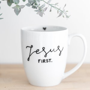 Könnte beinhalten: Weiße Keramiktasse mit einer schwarzen, kursiv geschriebenen Aufschrift "Jesus First."