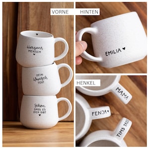 Könnte beinhalten: Ein Set aus weißen Keramiktassen mit schwarzer Sprenkeloptik und schwarzem Textaufdruck. Die Tassen zeigen verschiedene Sprüche wie Herzensmensch, Dein Wunschtext und Schön, dass es dich gibt, sowie individuelle Beschriftungen auf den Henkeln.