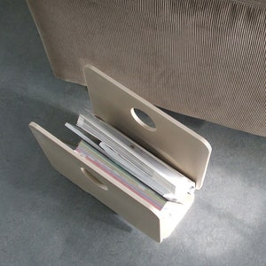 Può includere: Un porta riviste bianco con un design a taglio. Il porta riviste contiene una pila di riviste colorate.