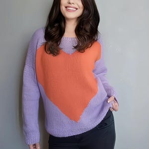 Könnte beinhalten: Ein lila Pullover mit einem großen orangefarbenen Herzdesign. Der Pullover hat lange Ärmel und einen Rundhalsausschnitt. Der Text "Yaren kaS" ist in Kursivschrift oben rechts geschrieben. Der Pullover ist aus weichem Strickmaterial.