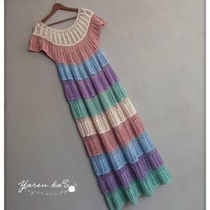 Pode incluir: Vestido longo de croch&ecirc; feito &agrave; m&atilde;o em cores pastel, incluindo rosa, azul, roxo e verde. O vestido tem um decote redondo e mangas curtas. O vestido est&aacute; pendurado em um cabide de madeira.