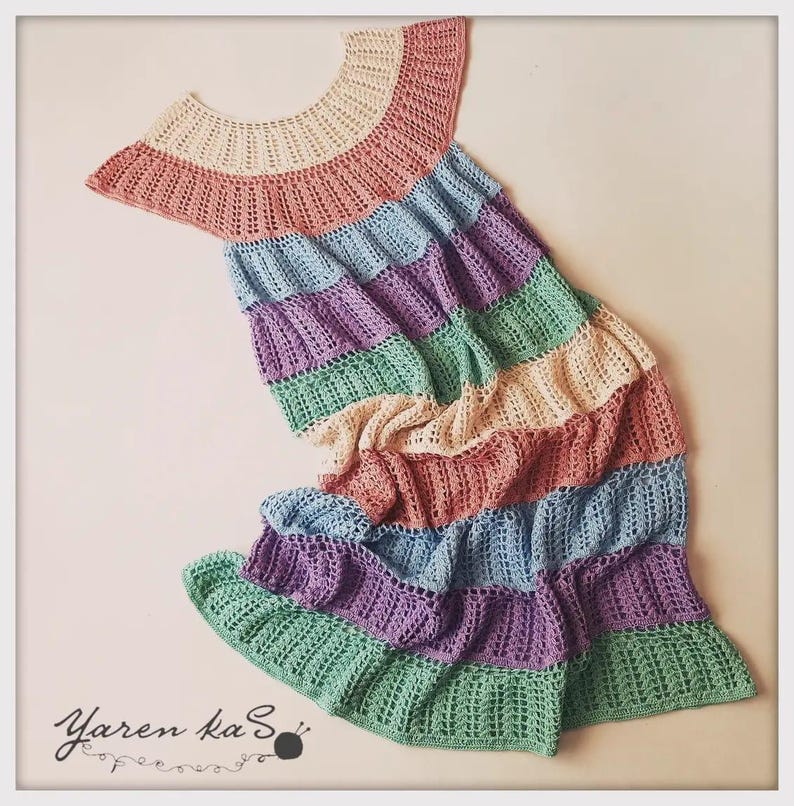 Pode incluir: Um vestido de croch&ecirc; feito &agrave; m&atilde;o, multicolorido, em tons pastel. O vestido apresenta um decote redondo e uma saia com babados em camadas. As cores incluem rosa, azul claro, roxo, verde e creme.