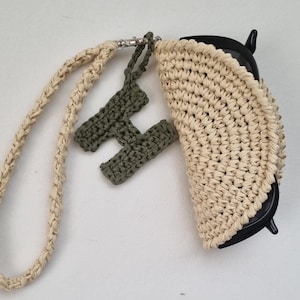 Può includere: Un astuccio per occhiali all'uncinetto color beige con cinturino da polso abbinato e un ciondolo a forma di lettera H all'uncinetto verde oliva scuro fissato da un moschettone in metallo argentato. L'astuccio contiene occhiali con montatura nera.