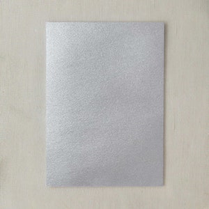 Pode incluir: Uma folha de papel de glitter prateado. O papel tem uma superfície texturizada e um brilho sutil.