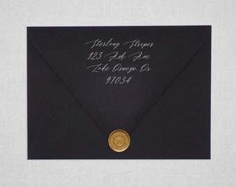 Può includere: Una busta nera con un'etichetta di indirizzo bianca che recita "Sterling Stripes, 123 Ash Ave, Lake Oswego, OR 97034". La busta è sigillata con un sigillo di cera dorato con un'iniziale "W".