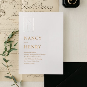 May include: A white wedding invitation with gold lettering. The invitation reads "Nancy and Henry are getting married Saturday, the Eighteenth of October Two Thousand Twenty-Two at Six O'Clock in the Evening Ritz-Carlton, Dallas, Texas Reception to Follow".
