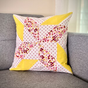Könnte beinhalten: Ein gelbes und rosafarbenes Kissen mit floralem Muster und weißen Punkten. Das Kissen liegt auf einem grauen Sofa.