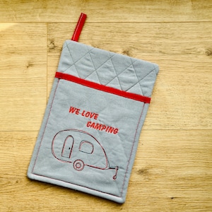 Könnte beinhalten: Grauer gesteppter Ofenhandschuh mit rotem Besatz und einer roten Stickerei eines Wohnwagens mit dem Text "We Love Camping".