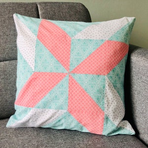 Könnte beinhalten: Ein Dekokissen mit einem geometrischen Muster in Rosa-, Grün- und Weißtönen. Das Kissen hat ein Sternmuster mit Dreiecken und Kreisen.