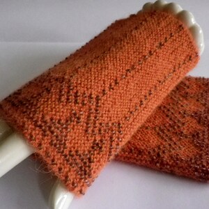 Könnte beinhalten: Ein Paar orangefarbene gestrickte Handgelenkswärmer mit einem dezenten Perlmuster.