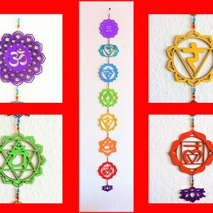 Könnte beinhalten: Ein Wandbehang aus Holz mit sieben bunten Chakra-Symbolen, jedes mit einem einzigartigen Design und einer Farbe. Die Symbole sind durch eine Perlenkette verbunden, und das untere Symbol ist eine violette Lotusblume.