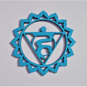 May include: A teal blue wooden mandala with a white symbol in the centre. The symbol is a stylised representation of the fifth chakra, the throat chakra, which is associated with communication and expression.