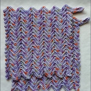 Könnte beinhalten: Eine gehäkelte Decke mit einem Zickzackmuster in den Farben Lila, Orange und Grün.