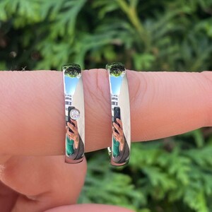 May include: Two silver wedding bands, one with a small diamond, worn on a finger.