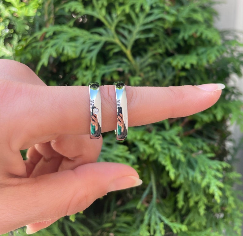 May include: Two silver wedding bands, one with a small diamond, worn on a finger.