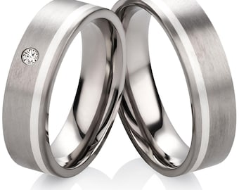 May include: A pair of silver wedding bands with a white inlay. One band features a small diamond.