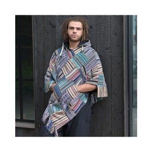 Peut inclure: Un poncho à capuche avec un motif patchwork présentant des motifs géométriques dans des tons de bleu, marron, beige et rouge. Le poncho a des franges sur les bords et une fermeture éclair.