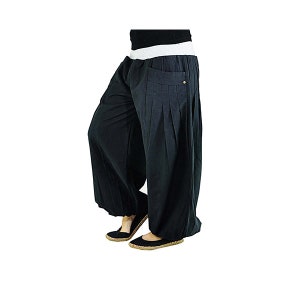May include: Black harem pants with a wide, white waistband and pleated front pockets. The loose-fitting pants have a relaxed silhouette and are paired with black flats. The pants are made of a soft, flowing fabric.