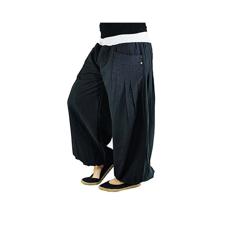 May include: Black harem pants with a wide, white waistband and pleated front pockets. The loose-fitting pants have a relaxed silhouette and are paired with black flats. The pants are made of a soft, flowing fabric.