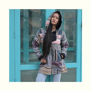 Könnte beinhalten: Eine langärmelige Kapuzenjacke mit Patchwork-Design, das verschiedene geometrische Muster in Schwarz, Weiß, Braun, Rosa, Blau und Grün zeigt. Die Jacke hat einen Reißverschluss und zwei Taschen.