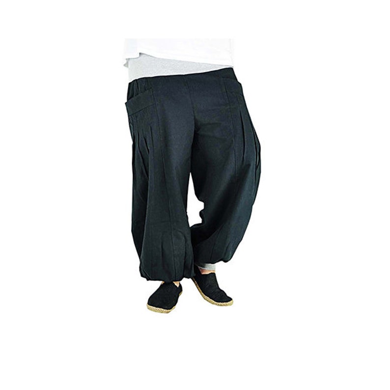 May include: Black harem pants with a relaxed fit. The pants have a high waist, pleats, and pockets. The ankles are gathered. The person is wearing black shoes. The pants are made of a soft, flowing fabric.