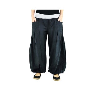 May include: Black harem pants with a wide, pleated design. The pants have large pockets and a gray waistband. The model is wearing black flats. These comfortable pants are suitable for casual wear.