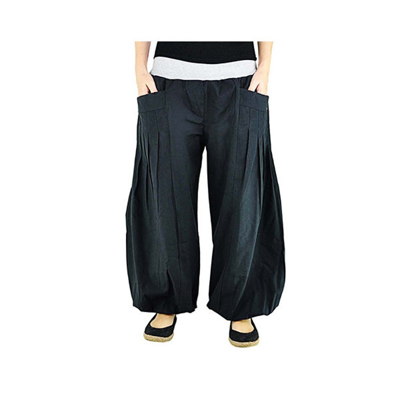 May include: Black harem pants with a wide, pleated design. The pants have large pockets and a gray waistband. The model is wearing black flats. These comfortable pants are suitable for casual wear.