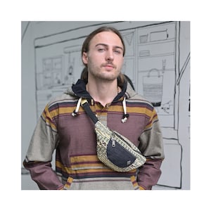 Op de afbeelding: Een persoon draagt een gestreept, getailleerd shirt met een zwart en geel gepatroneerd heuptasje dat over de borst wordt gedragen.