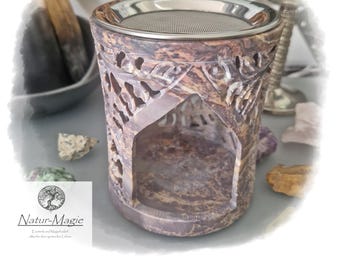 May include: A carved stone aromatherapy diffuser with a metal mesh top. The diffuser is a mix of purple, brown, and tan colors. The front of the diffuser has an arched opening. The text "Natur-Magie" is visible on a white label.