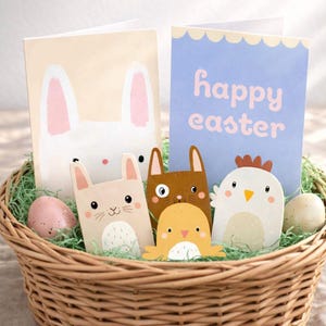 Könnte beinhalten: Ein Weidenkorb gefüllt mit Osterdekorationen. Enthält Grußkarten mit Hase und dem Text "Frohe Ostern", sowie Holzausschnitte eines Hasen, einer Katze, eines Küken und eines Huhns. Dekorative Eier und grüne Füllung vervollständigen die Szene.