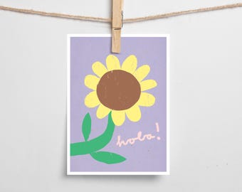 Könnte beinhalten: Eine farbenfrohe Illustration einer Sonnenblume mit gelben Blütenblättern und einem braunen Zentrum, grünem Stiel und Blättern sowie dem Wort "hola!" in Rosa auf einem lila Hintergrund. Das Kunstwerk wird von einer Holzklammer gehalten und an einer Schnur aufgehängt.