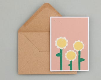 Könnte beinhalten: Eine rosa Karte mit weißem Rand zeigt drei weiße Blumen mit gelben Zentren und grünen Stielen. Die Blumen sind in einer Gruppe auf der Karte angeordnet.