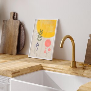 Może przedstawiać: Abstrakcyjny obraz w ramie z ż&oacute;łtym słońcem, zielonymi liśćmi i r&oacute;żowymi i niebieskimi kwiatami. Obraz wisi na ścianie nad drewnianym blatem.