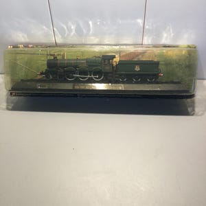 May include: A green and black model train engine with gold accents. The engine is in a clear plastic display case with a black base.