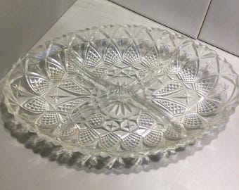 May include: Clear glass serving dish with three compartments. The oval-shaped dish features a detailed, textured pattern of geometric shapes and a scalloped edge. Ideal for serving snacks or appetizers.