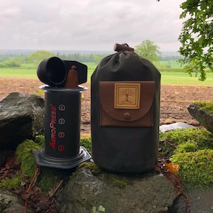 May include: A black AeroPress coffee maker with a brown leather carrying case. The case has a tree logo on the front.