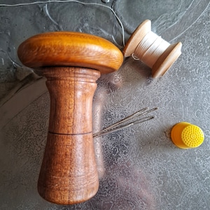 Könnte beinhalten: Ein hölzerner Fingerhut mit einem pilzförmigen Oberteil, eine Spule weißen Fadens und ein gelber Fingerhut mit einer strukturierten Oberfläche.