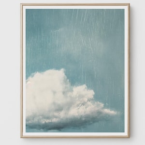 Könnte beinhalten: Ein gerahmter Kunstdruck mit einem strukturierten Gemälde einer einzelnen großen weißen Wolke vor einem gedämpften blauen Himmel. Das Kunstwerk zeigt sichtbare vertikale Pinselstriche, die einen Effekt von leichtem Regen erzeugen.