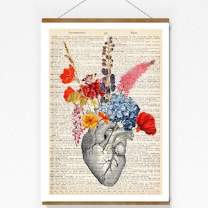 Könnte beinhalten: Gerahmter Druck mit einer grau gestuften anatomischen Herzillustration, gefüllt mit bunten Blumen. Die Blumen umfassen rote Mohnblumen, blaue Hortensien und gelbe und orangefarbene Blüten. Der Hintergrund ist eine Vintage-Wörterbuchseite.